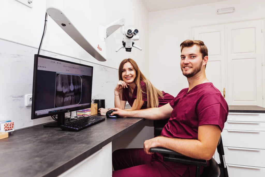 U stolu v moderní zubní ordinaci sedí dva zubaři v kaštanových peelingech. Zkoumají rentgeny zubů na monitoru počítače. Nad hlavou je namontován mikroskop a světlá místnost vyzařuje profesionalitu. Oba se usmívají do kamery a předvádějí své přívětivé dentální centrum.